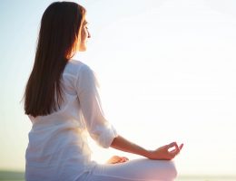 Side view of meditating woman sitting in pose of lotus against clear sky outdoors